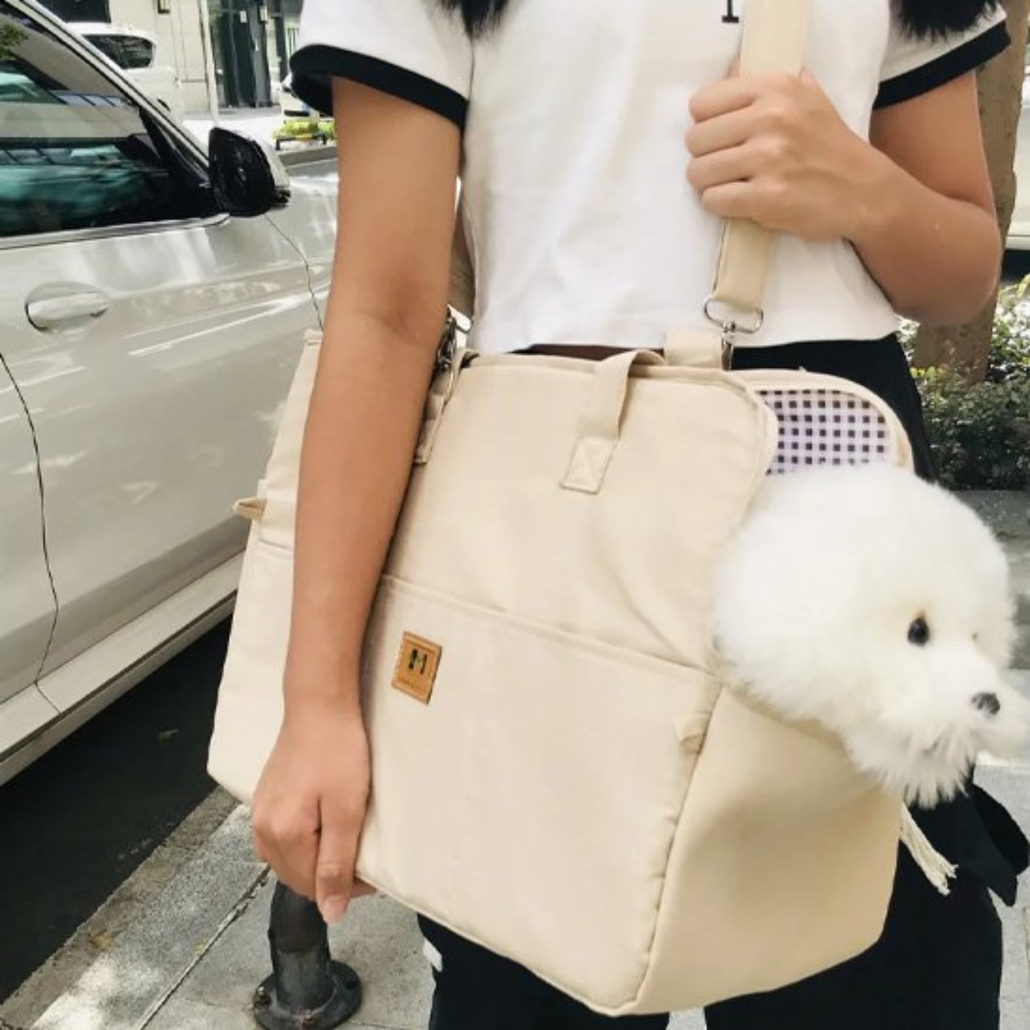 Sac voiture pour chien beige porté en bandoulière, chien blanc sortant la tête.